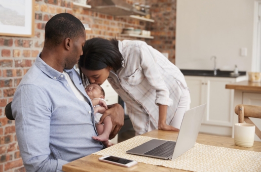 Father Working On Laptop Holds Newborn Son With Mother