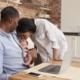 Father Working On Laptop Holds Newborn Son With Mother