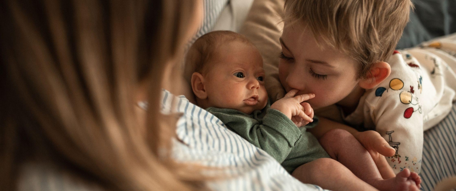 A newborn baby is cuddled by their parent and older sibling. Like night nurses and night nannies, our team provide expert infant care while also offering support for the whole family.