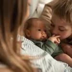 A newborn baby is cuddled by their parent and older sibling.