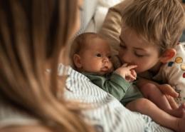 A newborn baby is cuddled by their parent and older sibling.