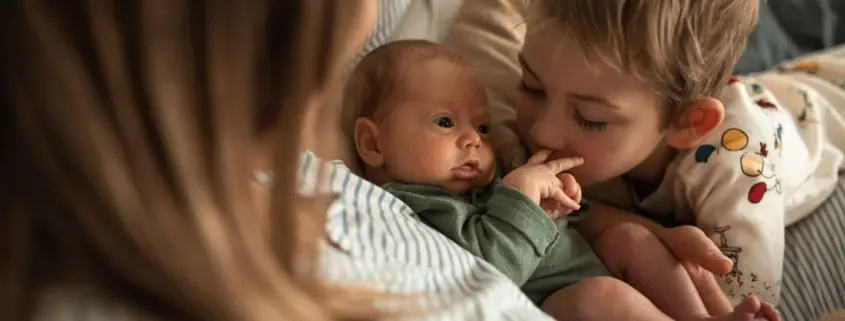 A newborn baby is cuddled by their parent and older sibling.