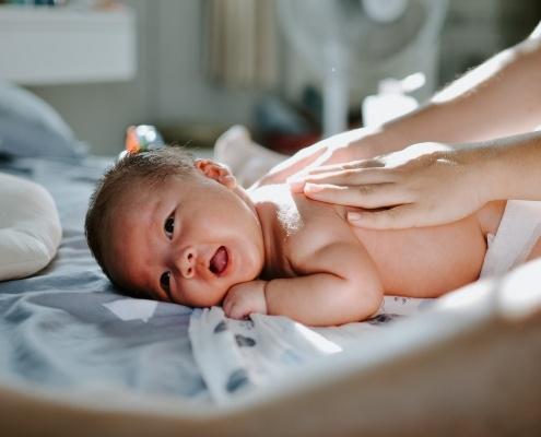 white newborn baby lying belly down with two hands (belonging a person not in the frame) on the baby's back