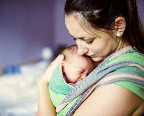 woman with dark hair holding a newborn baby in a sling