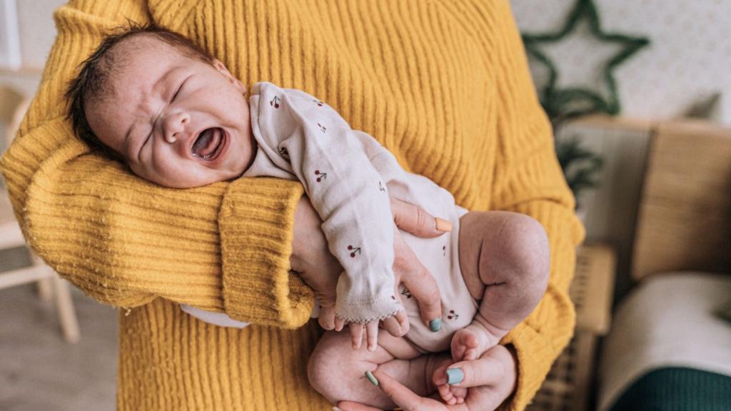 A baby is held by their caregiver and in distress as the caregiver attempts to soothe them.