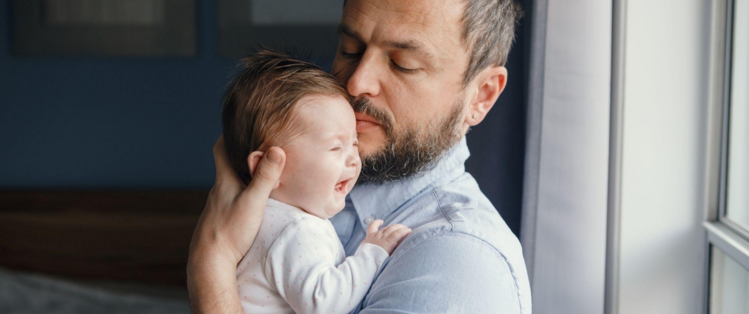 A father tries to soothe his baby as they cry in his arms.