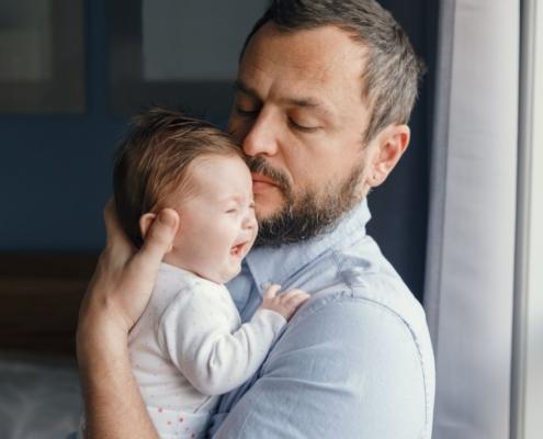 A father tries to soothe his baby as they cry in his arms.