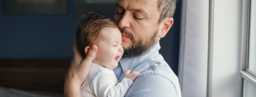 A father tries to soothe his baby as they cry in his arms.