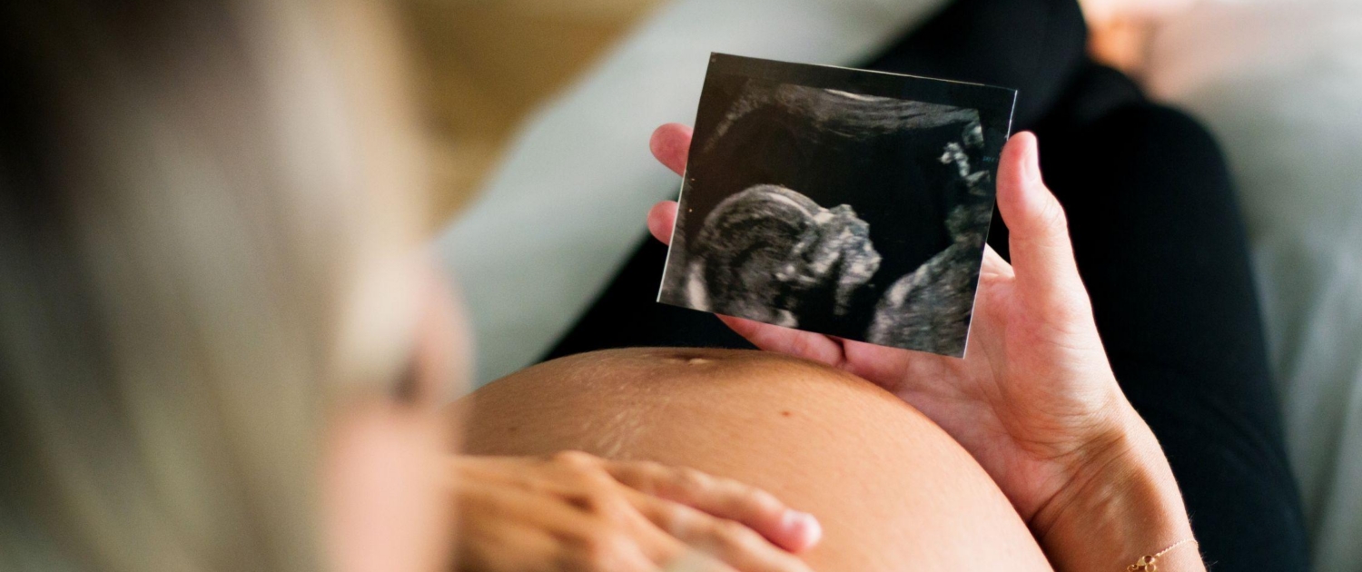 A pregnant person looks at their ultrasound photo while relaxing in their home.
