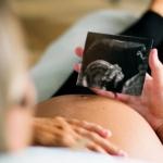 A pregnant person looks at their ultrasound photo while relaxing in their home.