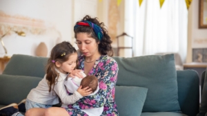 A mother introduces their older child to their new sibling.