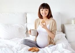 Pregnant person sitting on bed, smiling, enjoying cookies. Feeling prepared by childbirth education and birth doula support in Baltimore