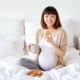 Pregnant person sitting on bed, smiling, enjoying cookies. Feeling prepared by childbirth education and birth doula support in Baltimore