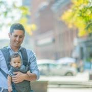 Parent with baby in front pack walking down Baltimore city street in summer
