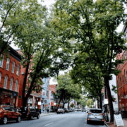 Downtown Frederick, MD street view shows brick buildings and tree-lined street.