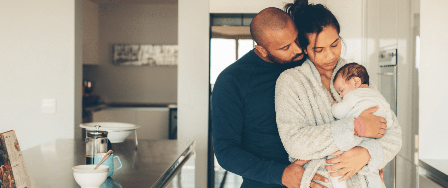 A couple looks at their newborn enjoying the postpartum time together in the kitchen.