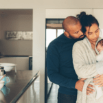 A couple looks at their newborn enjoying the postpartum time together in the kitchen.