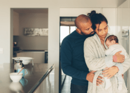 A couple looks at their newborn enjoying the postpartum time together in the kitchen.