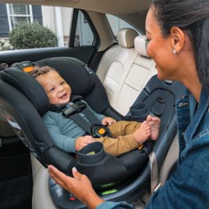 Chicco Fit 360 revolving carseat in the back seat of a car, caregiver is helping strap baby in properly
