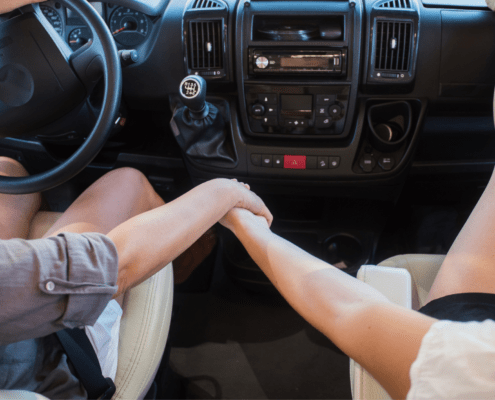 Two people hold hands in the front of a vehicle