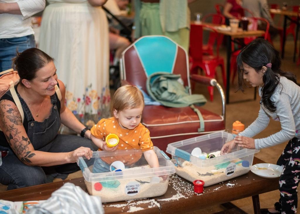 Little ones play with sensory bins alongside their caregivers.