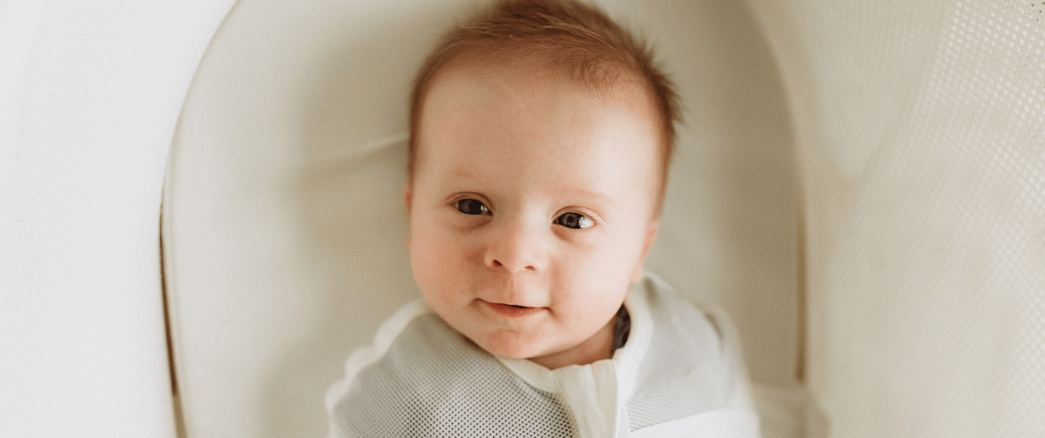 A baby smiles at a camera from a snoo bassinet