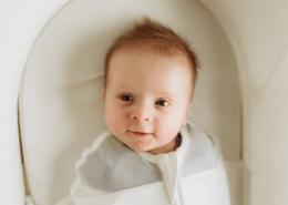 A baby smiles at a camera from a snoo bassinet