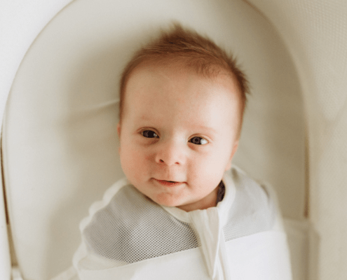 A baby smiles at a camera from a snoo bassinet