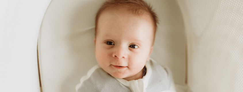 A baby smiles at a camera from a snoo bassinet