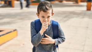 Young school-aged boy with backpack coughs.