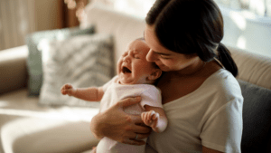 baby cries in mother's arms overwhelmed from meeting friends and family