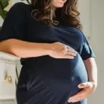 A pregnant person cradles their belly as they contemplate the changes in their body once their baby arrives.