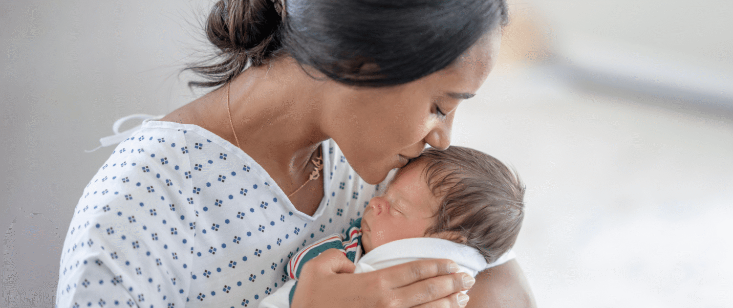A mother kisses her newborn with moderate head molding.