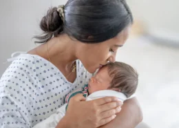 A mother kisses her newborn with moderate head molding.
